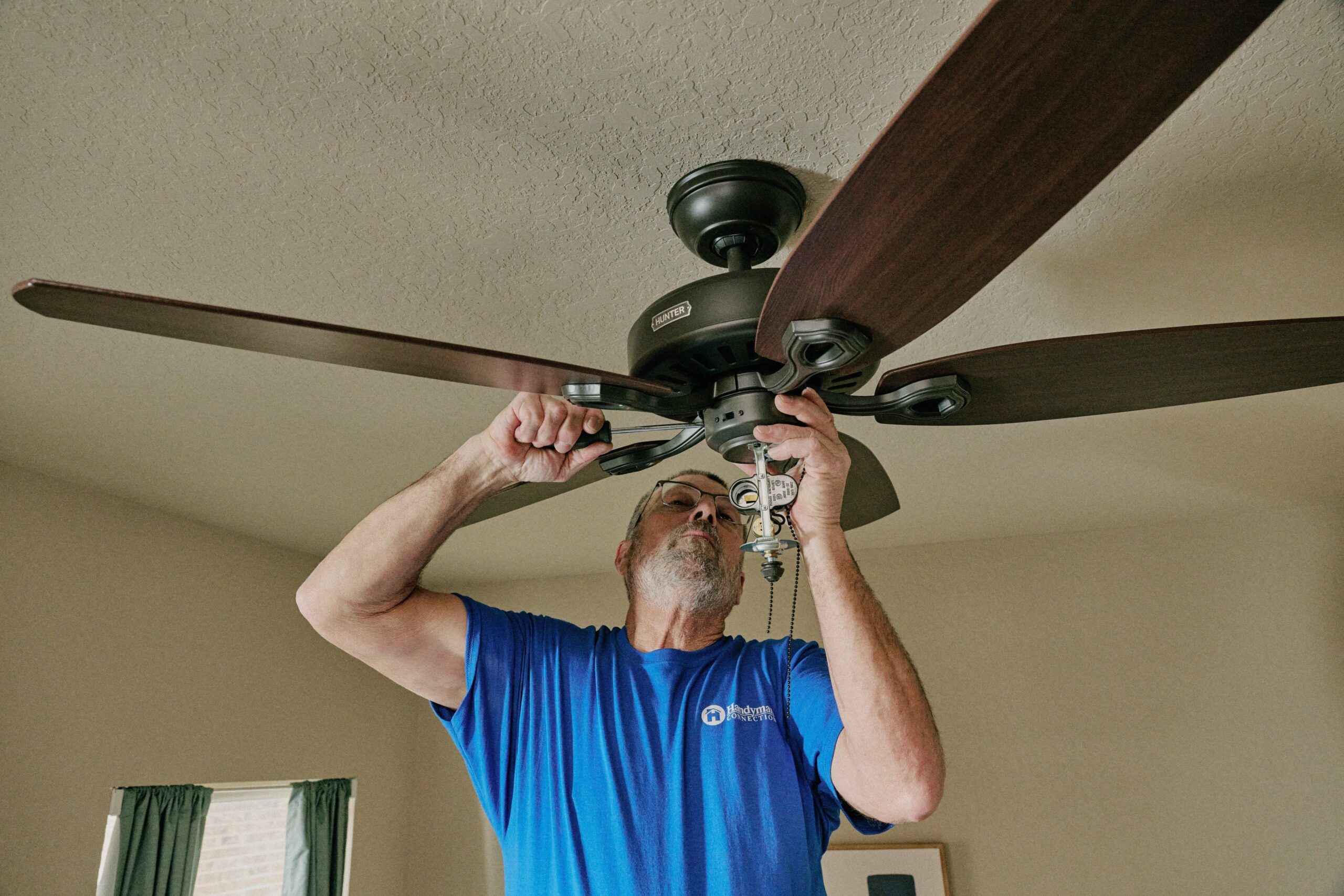 local handyman installing ceiling fan inside home